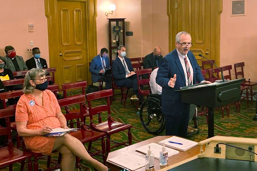 Tim Young stands at a podium delivering remarks in a sparsely populated room in the Ohio Statehouse.
